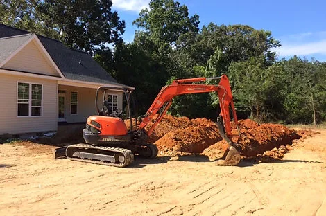 Orange compact excavator digging near a new single-story house on a graded lot