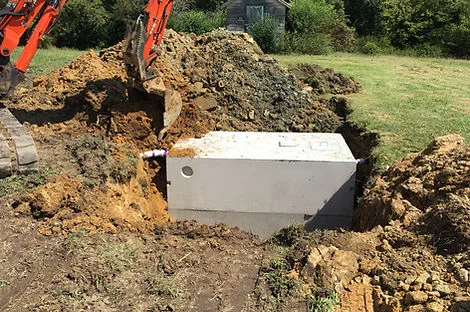 Concrete septic tank in an open excavation beside piles of excavated soil