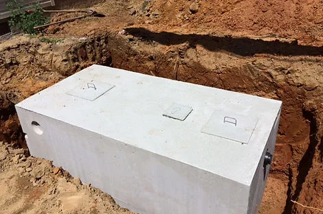 Concrete septic tank with two access lids set in a red clay excavation