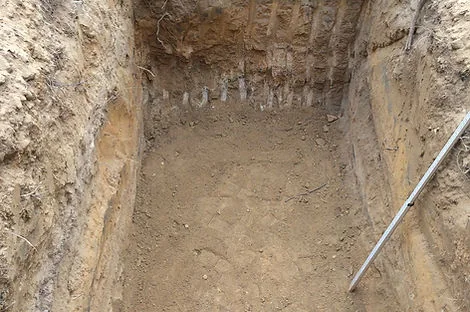 Deep rectangular excavation in tan clay soil with a measuring rod leaning in the corner Deep rectangular excavation in tan clay soil with a measuring rod leaning in the corner