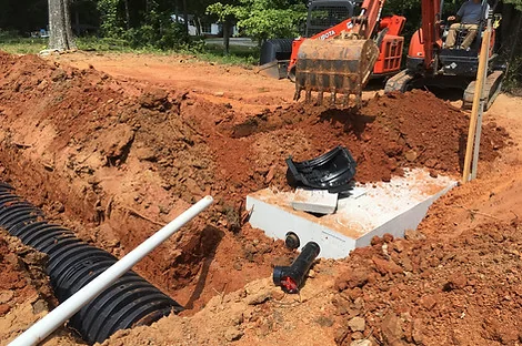 Distribution box with white PVC lines leading to a chamber trench while an excavator works behind Distribution box with white PVC lines leading to a chamber trench while an excavator works behind