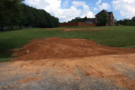 Graded red clay pad with a pile of spoil on a lawn