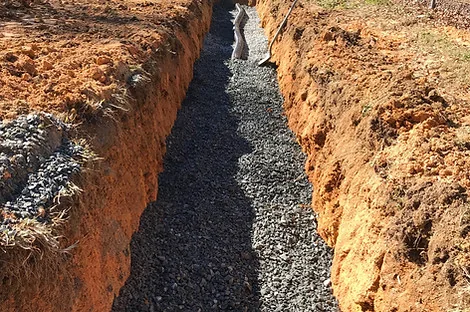 Gravel bed laid in a narrow drain field trench cut through red clay Gravel bed laid in a narrow drain field trench cut through red clay