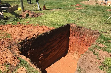 Square test pit dug in a lawn exposing red clay layers Square test pit dug in a lawn exposing red clay layers