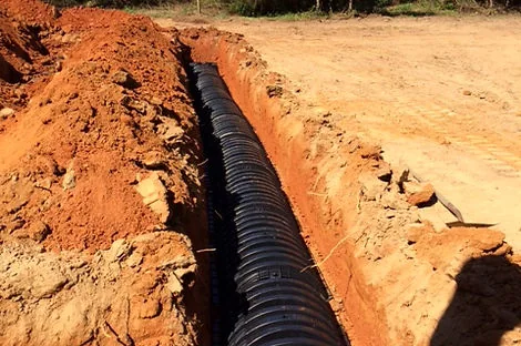 Black plastic drain field chambers laid end to end in a red clay trench