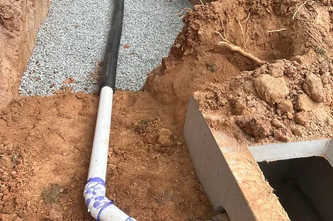 White PVC pipe with a primed elbow leading to a concrete box beside a gravel bed White PVC pipe with a primed elbow leading to a concrete box beside a gravel bed