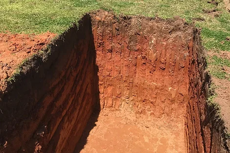 Deep pit cut into red clay showing the vertical soil profile on the wall
