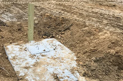 Concrete septic tank lid at ground level marked with a wood stake