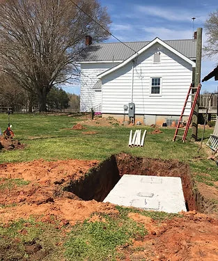 Concrete septic tank set in an open excavation beside a white farmhouse Concrete septic tank set in an open excavation beside a white farmhouse