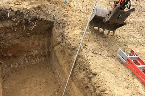 Soil test pit with visible soil layers and an excavator bucket at the edge Soil test pit with visible soil layers and an excavator bucket at the edge